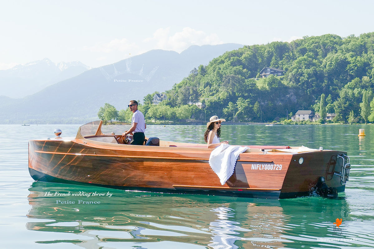 Bateau en bois élégant sur lac calme avec deux passagers, montagne et forêts en arrière-plan.