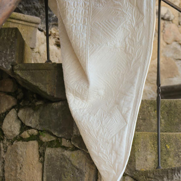 Serviette blanche délicatement drapée sur un balcon en pierre, motifs géométriques et reliefs visibles.