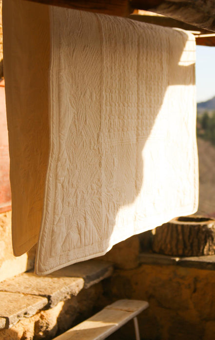 Serviette blanche suspendue à l’extérieur pour sécher au soleil, près d’un mur en pierre et d’un rebord en bois.