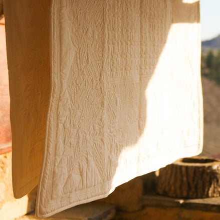 Serviette blanche suspendue à l’extérieur pour sécher au soleil, près d’un mur en pierre et d’un rebord en bois.