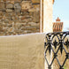 Dentelle blanche suspendue sur une balustrade en fer forgé devant un mur en pierre et une lanterne, style balcon provençal.