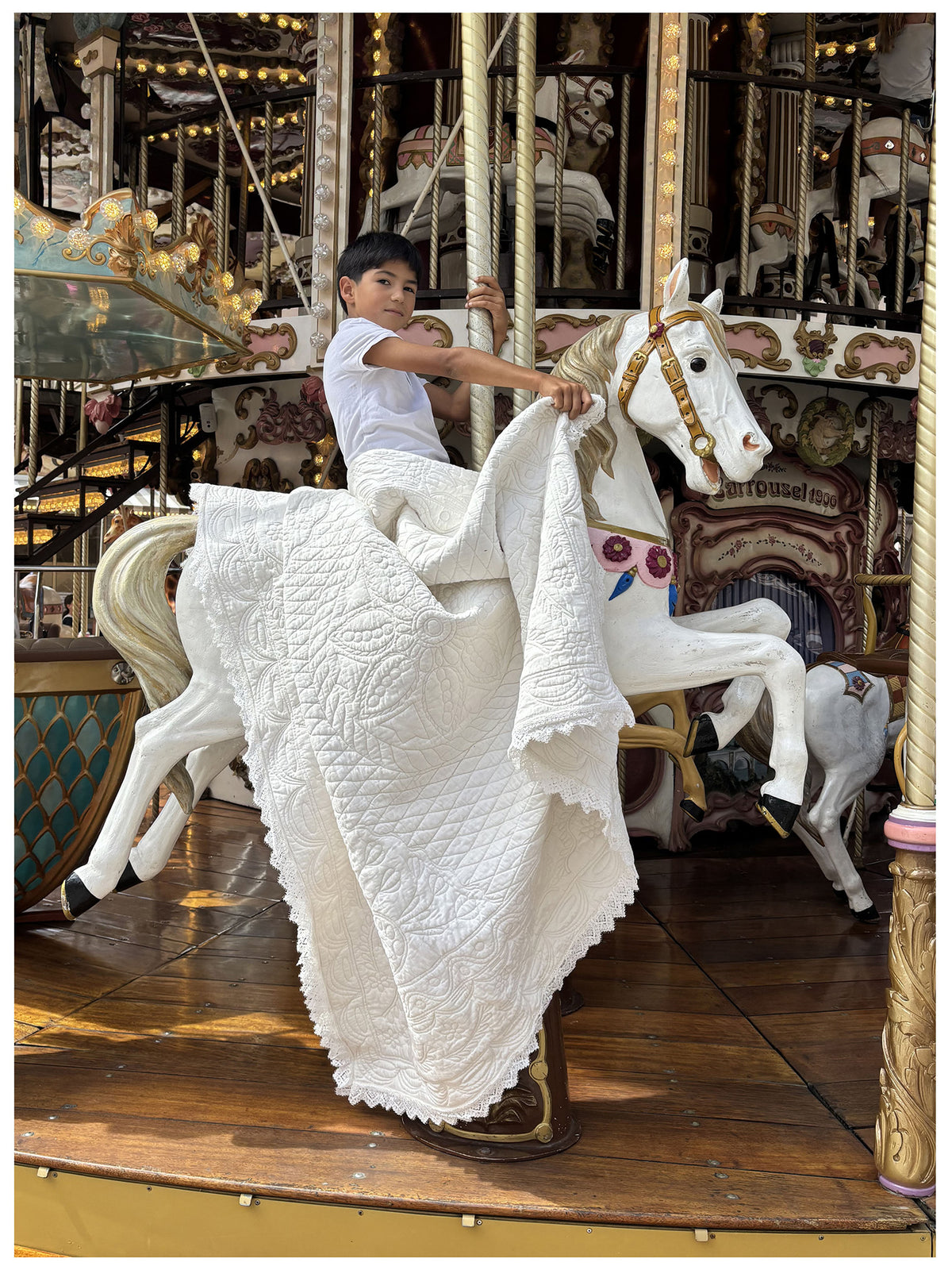 Jeune garçon sur un cheval de manège blanc, vêtu d’un voile blanc et d’un chevalier rideau décoratif, au haut du manège.