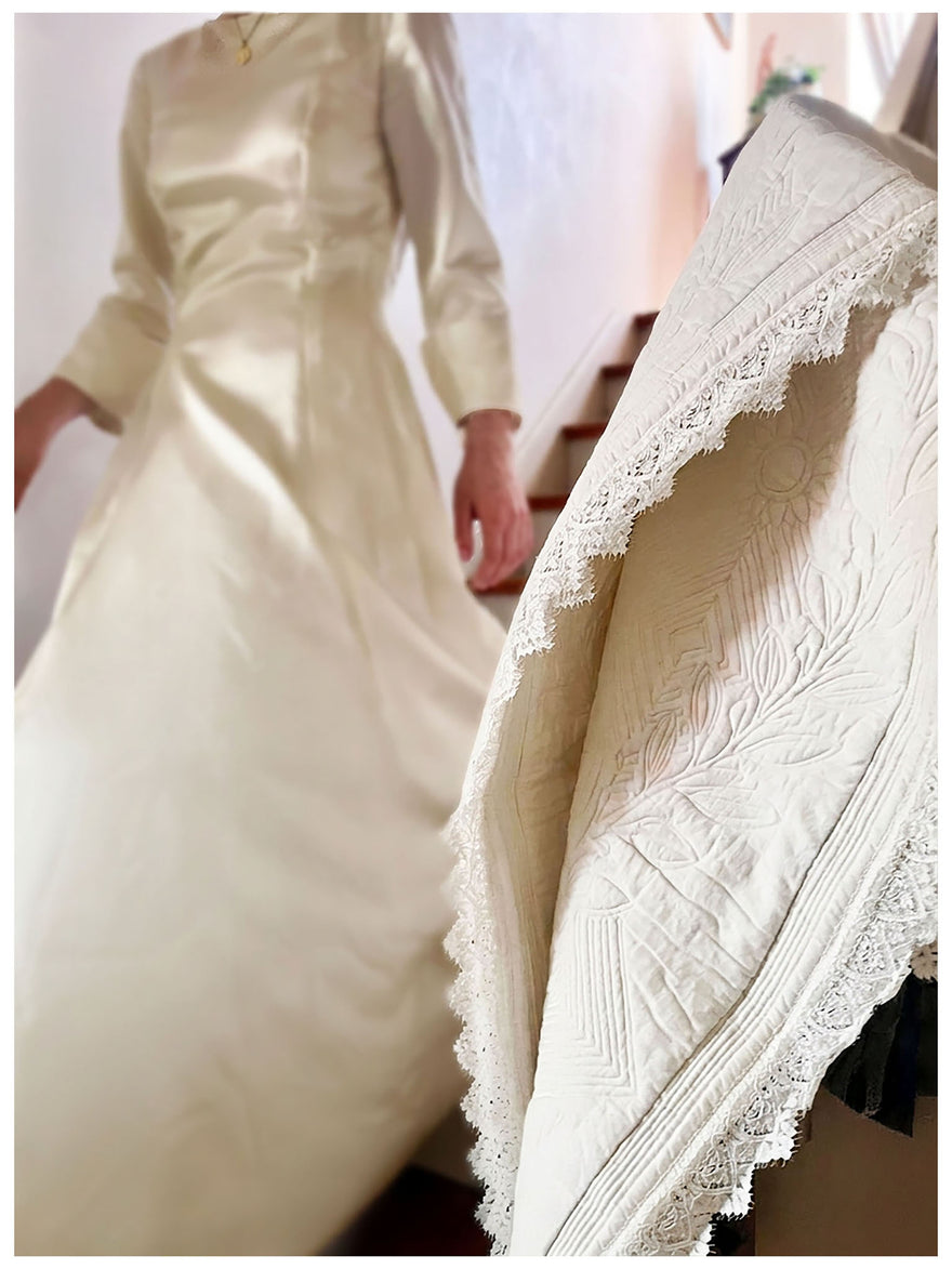 Vêtement de mariée blanc cassé avec dentelle sur la traîne, dans une boutique; texte « Le carré de mariage Petite France ».