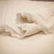Dentelle blanche sur couverture ou drap beige, motif délicat et texture tissée, with rolled edge detail.