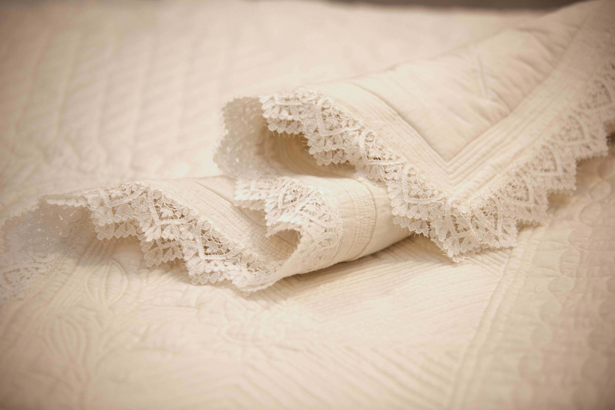 Dentelle blanche sur couverture ou drap beige, motif délicat et texture tissée, with rolled edge detail.