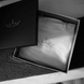 Caillebotis noir et boîte cadeau ouverte révélant un édredon ou couverture blanche, témoin d’un emballage élégant. Keywords: boîte cadeau.
