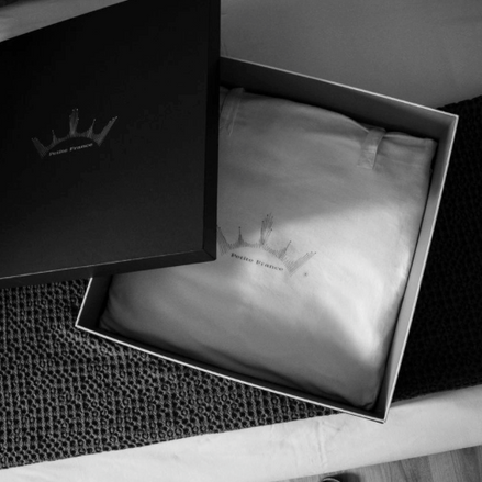 Caillebotis noir et boîte cadeau ouverte révélant un édredon ou couverture blanche, témoin d’un emballage élégant. Keywords: boîte cadeau.