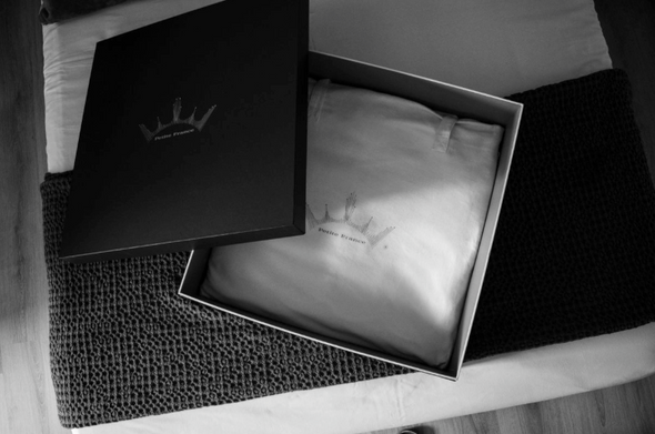 Caillebotis noir et boîte cadeau ouverte révélant un édredon ou couverture blanche, témoin d’un emballage élégant. Keywords: boîte cadeau.