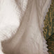 Voilage ou couverture blanche à motif discret, bordure en dentelle près d’un tissu d’ameublement vert et doré.