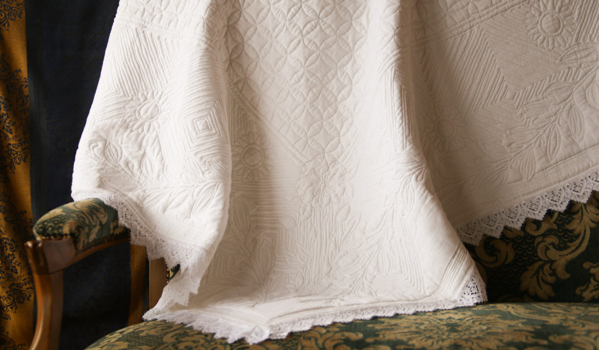 Couverture en dentelle blanche légère posée sur un canapé vert et doré à motif, avec bordures festonnées visibles.