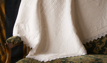 Couverture en dentelle blanche légère posée sur un canapé vert et doré à motif, avec bordures festonnées visibles.