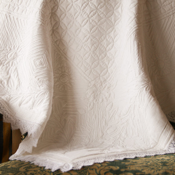 Couverture en dentelle blanche légère posée sur un canapé vert et doré à motif, avec bordures festonnées visibles.