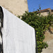 Linge blanc accroché au-dessus d’une barrière métallique, séchant au soleil sur fond de mur et de végétation.
