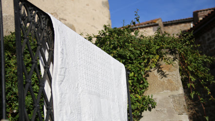 Linge blanc accroché au-dessus d’une barrière métallique, séchant au soleil sur fond de mur et de végétation.