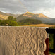 Couverture quiltée blanche drapée sur une rambarde avec vue sur montagnes, prairie et arc-en-ciel tôt le matin.