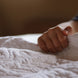 Mains d’un enfant sur une couverture quiltée, doigts serrés près du bord du drap blanc.