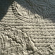 Textile brillant avec motifs quiltés: fleurs, feuilles et motifs organiques en relief, jeu de lumière et ombres.