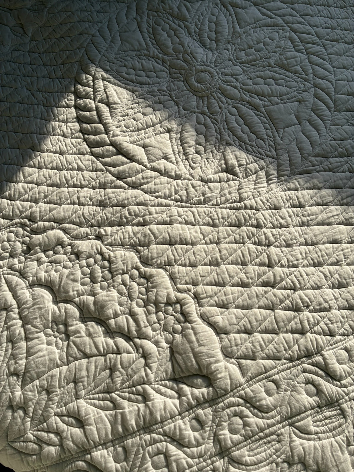 Textile brillant avec motifs quiltés: fleurs, feuilles et motifs organiques en relief, jeu de lumière et ombres.