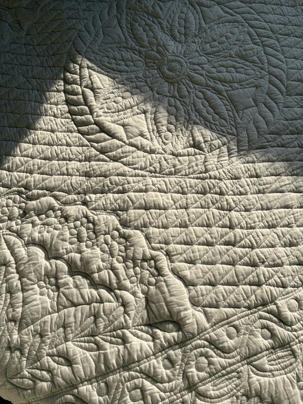 Textile brillant avec motifs quiltés: fleurs, feuilles et motifs organiques en relief, jeu de lumière et ombres.