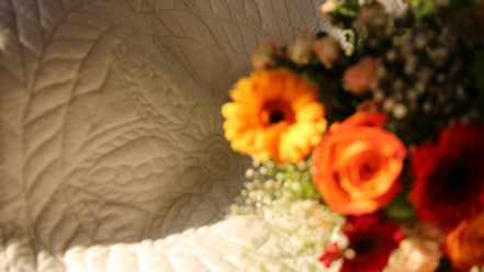 Bouquet de fleurs aux couleurs orange et rouge posé sur un drap clair texturé.
