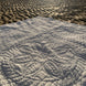 Une couverture ou tapis blanc à motifs circulaires gravés sur le sable d’une plage au coucher du soleil.