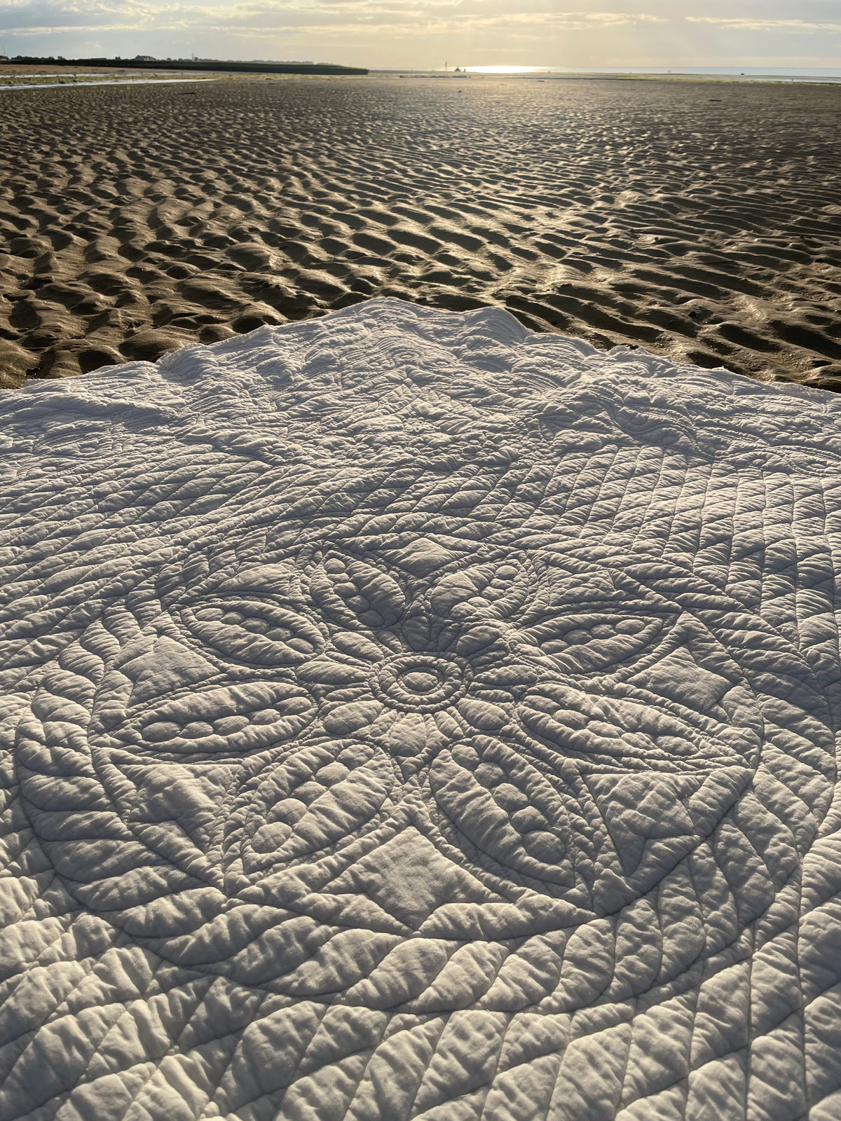 Une couverture ou tapis blanc à motifs circulaires gravés sur le sable d’une plage au coucher du soleil.