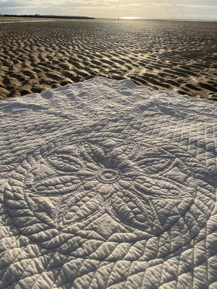 Une couverture ou tapis blanc à motifs circulaires gravés sur le sable d’une plage au coucher du soleil.