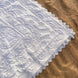 Dentelle blanche à motifs floraux et géométriques posée sur sable, bordure en dentelle fine.