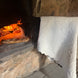 Pain de pain posé dans un four à bois allumé, couvert d’une nappe blanche décorée.