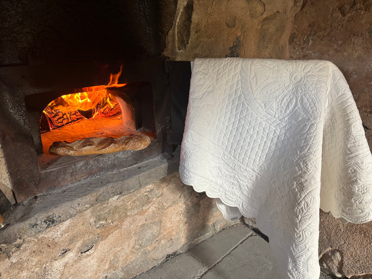 Pain de pain posé dans un four à bois allumé, couvert d’une nappe blanche décorée.