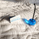 Boucle bleue avec tige noire sur une couette rembourrée; étiquette d’entretien et symbole de lavage à côté.