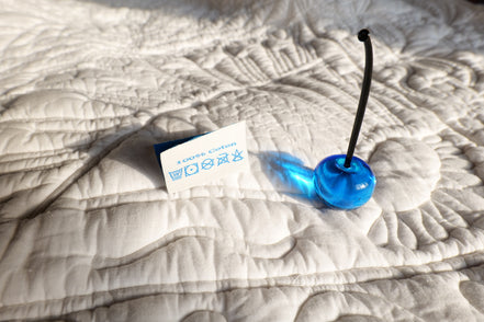 Boucle bleue avec tige noire sur une couette rembourrée; étiquette d’entretien et symbole de lavage à côté.