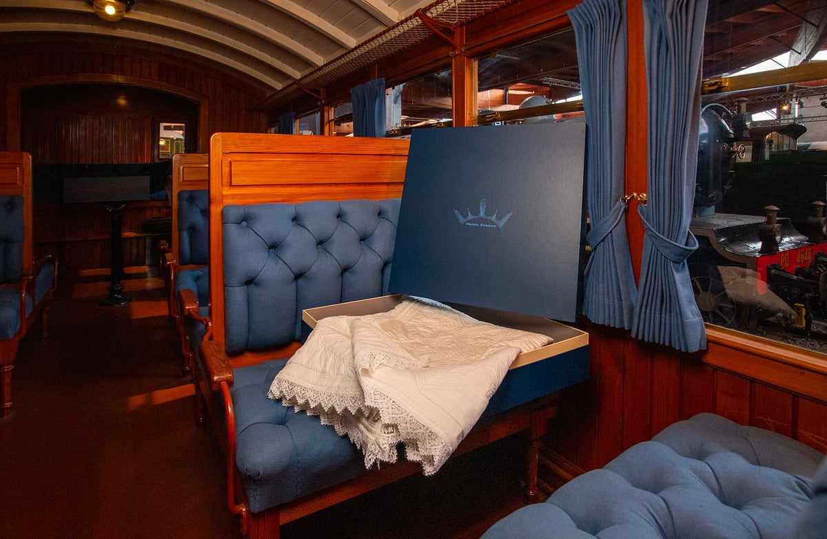 Bureau secret d’un wagon-lits avec banquette bleu et rideaux bleus, présentoir noir posé, linge blanc posé dessus.