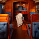 Intérieur d'un wagon-restaurants ou compartimentées en bois, banquettes bleues, tissu tufté et rideaux bleus, avec une couverture blanche posée sur le sol.