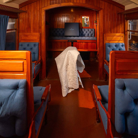 Intérieur d'un wagon-restaurants ou compartimentées en bois, banquettes bleues, tissu tufté et rideaux bleus, avec une couverture blanche posée sur le sol.