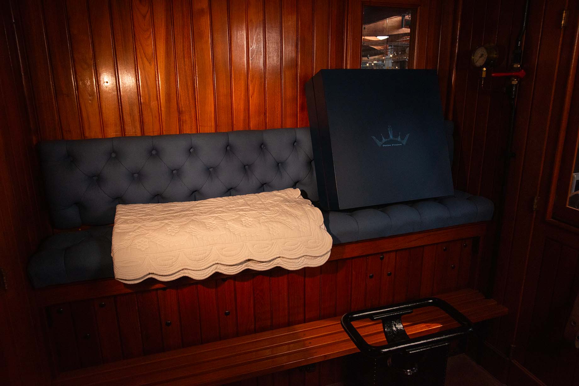 Banquette en bois vernie avec coussin bleu et traversin blanc dans une cabine, appareil de sauna posé dessus.
