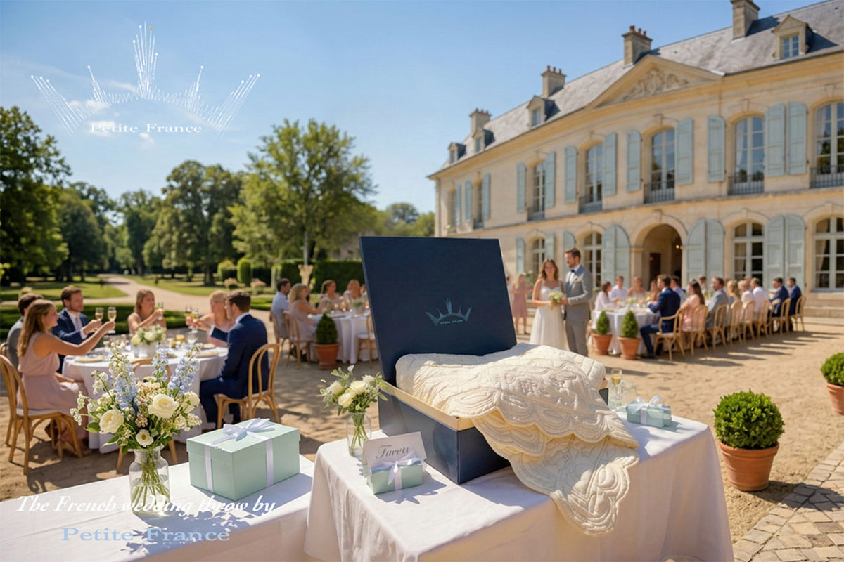 Mariage en plein air devant un manoir élégant, tables dressées et invités célébrant, avec une grande boîte cadeau et voile de mariée sur une table au premier plan.