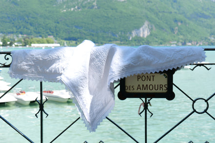 Charmant drapé blanc posé sur une balustrade près d’un lac alpin, avec le panneau “Pont des Amours” en arrière-plan.