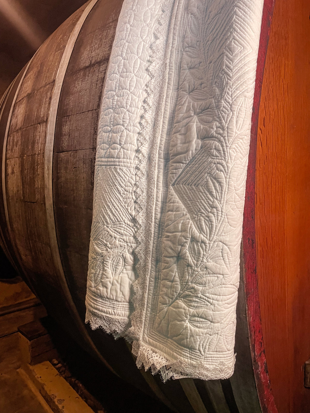Tronc d’un tonneau en bois avec des linges ou textiles blancs brodés drapés sur le bord, motifs quiltés et dentelle en bas.