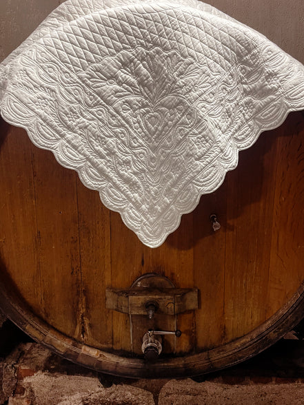 Cuve en bois d’un tonneau avec nappe blanche brodée couvrant le dessus. Détails du robinet et du métal au bas.