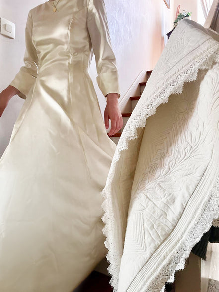 Personne en robe de mariée ivoire, haut ajusté et manches trois quarts, descend les marches près d’une table ornée d’un linge blanc à dentelle.